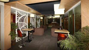 A modern indoor space with wooden paneling, a patterned partition, and seating areas with tables and chairs.