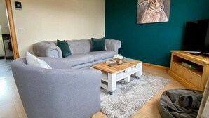 Un salon moderne avec un canapé gris, une table basse en bois et un mur d’accent de couleur turquoise.