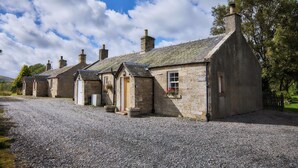 A row of stone cottages with a gravel driveway, each with a chimney and a small porch. - Mauldslie Hill Cottage (Gorebridge)