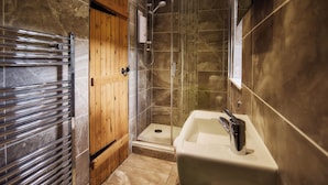A modern bathroom with a glass-enclosed shower, a wooden door, and a white sink. - Mauldslie Hill Cottage (Gorebridge)