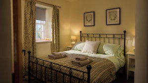 A neatly made bed with a patterned blanket and pillows, a bedside lamp, and a window with curtains. - Mauldslie Hill Cottage (Gorebridge)