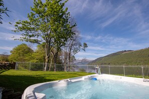 A hot tub in a backyard with a stone wall, a metal fence, and a view of a mountain.