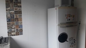 A kitchen with a refrigerator, microwave, and a wall with vintage-style tiles. - Casa Temporada Campeche (Florianópolis)