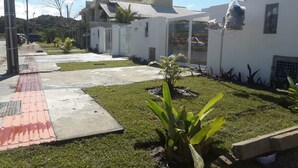 A residential area with a paved walkway, a small garden with a plant, and a modern building with a tiled roof. - Casa Temporada Campeche (Florianópolis)