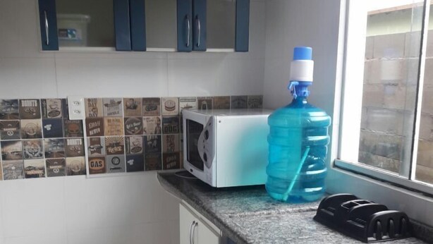 A kitchen with dark blue cabinets, a microwave, a large water bottle, and a black toaster on the counter. - Casa Temporada Campeche (Florianópolis)