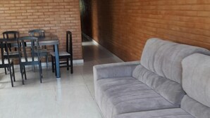 A modern living room with a grey sofa, a dining table with chairs, and a brick wall. - Casa Temporada Campeche (Florianópolis)