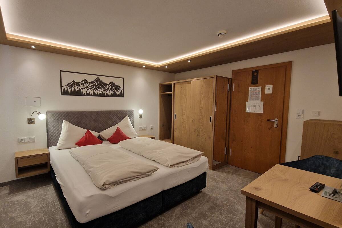 A hotel room with a bed, bedside tables, a desk, and a wardrobe.