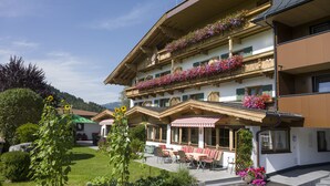 A multi-story building with balconies adorned with flowers, outdoor seating, and a garden area. - Tannenhof (Kirchberg in Tirol)