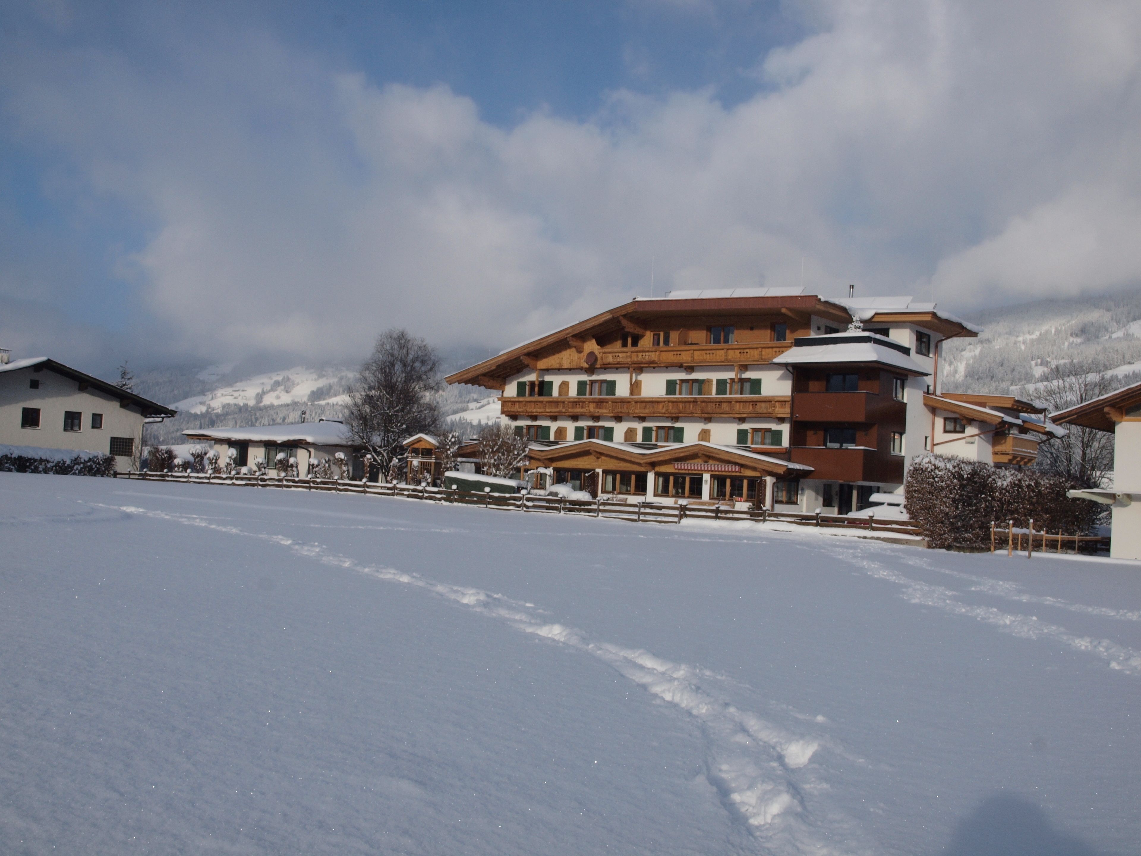 Paisagem coberta de neve com um edifício de vários andares, varandas e um centro de esqui ao fundo.