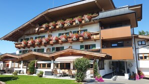 A multi-story hotel with balconies adorned with flowers, outdoor seating, and a well-maintained garden. - Tannenhof (Kirchberg in Tirol)
