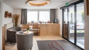 A reception area with a wooden desk, two grey armchairs, a bench, and a large window with curtains. - Tannenhof (Kirchberg in Tirol)