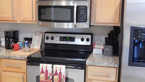 A kitchen with a stainless steel microwave, a black stove, wooden cabinets, and a refrigerator.