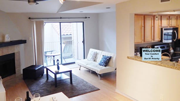 A modern living room with a fireplace, a sofa, a coffee table, and a dining area with a kitchen visible through an open door.