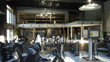 Un gimnasio con varios equipos de ejercicio, un reloj digital y un cartel que muestra la hora.