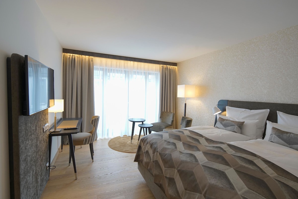 A hotel room with a large bed, a desk with a chair, a small table, and a TV mounted on the wall.