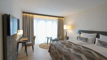 Una camera d'albergo con un letto grande, una scrivania con una sedia, un tavolino e una TV a muro.