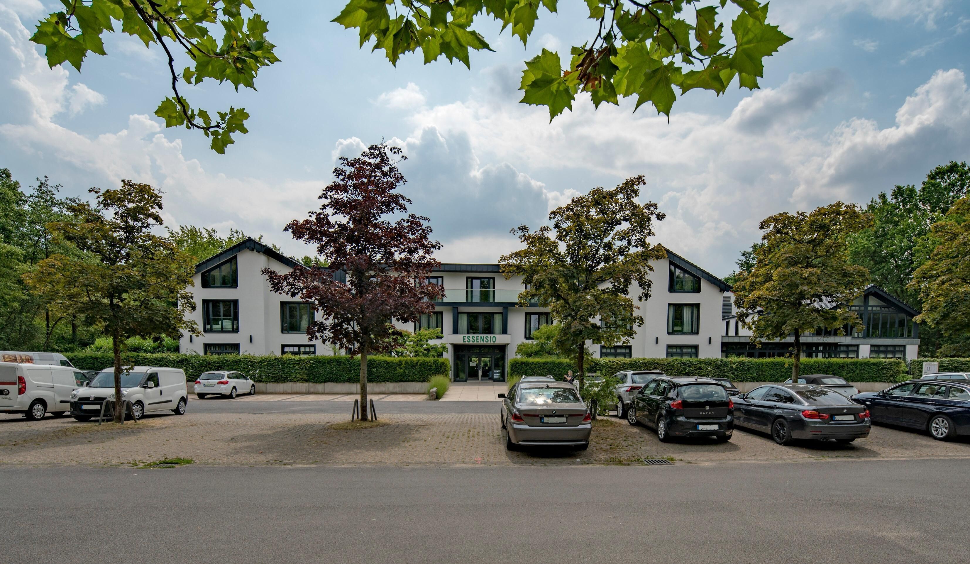 Ein modernes Gebäude mit einem Schild, auf dem "ESSENSIO" steht, und einem Parkplatz mit mehreren Autos.