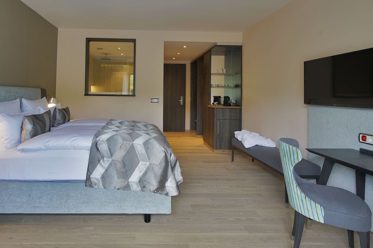 Una habitación de hotel moderna con una cama grande, un escritorio, una silla, un televisor y una kitchenette.