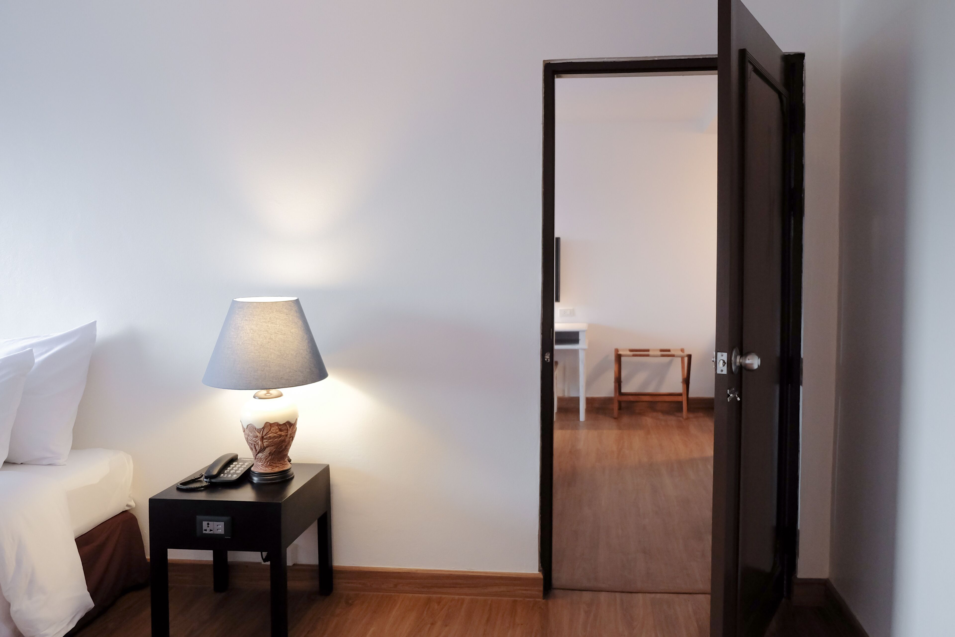 Ein Hotelzimmer mit einem Bett, einem Nachttisch mit Lampe, einem Telefon und einer Tür zu einem anderen Raum.