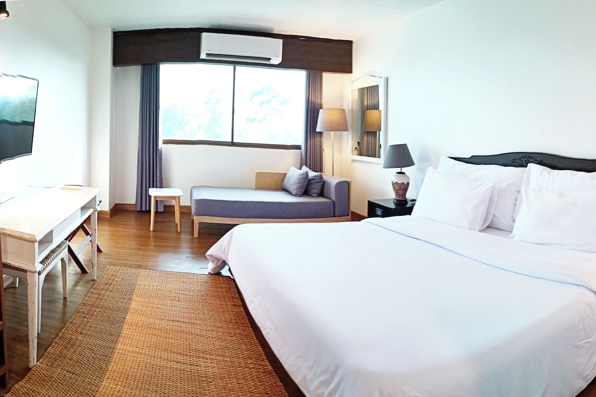 A hotel room with a bed, bedside table, lamp, and a desk with a chair.