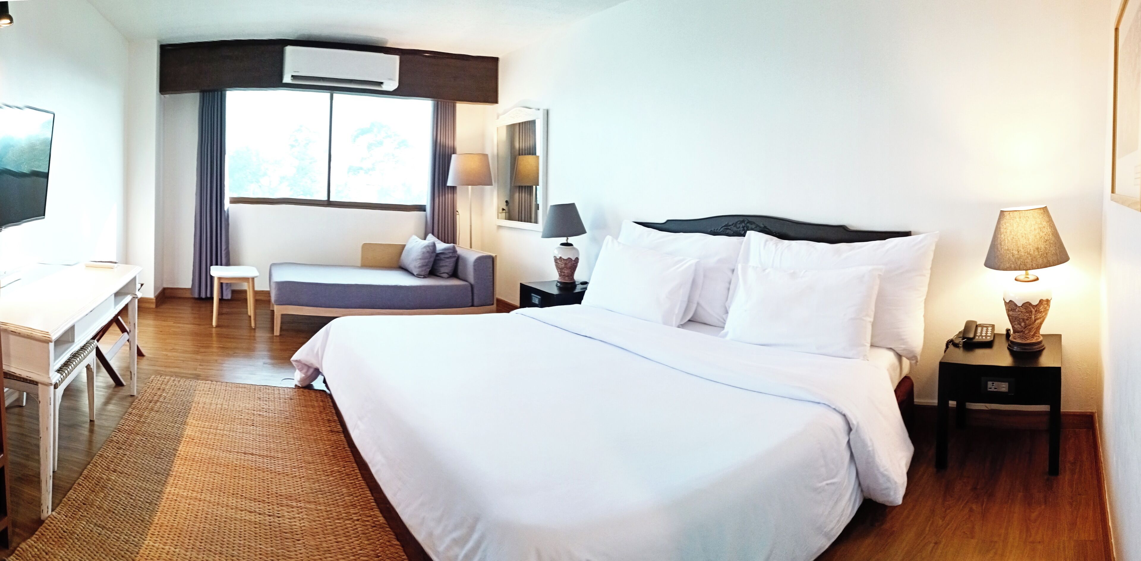 Een hotelkamer met een bed, nachtkastje, lamp en een bureau met stoel.