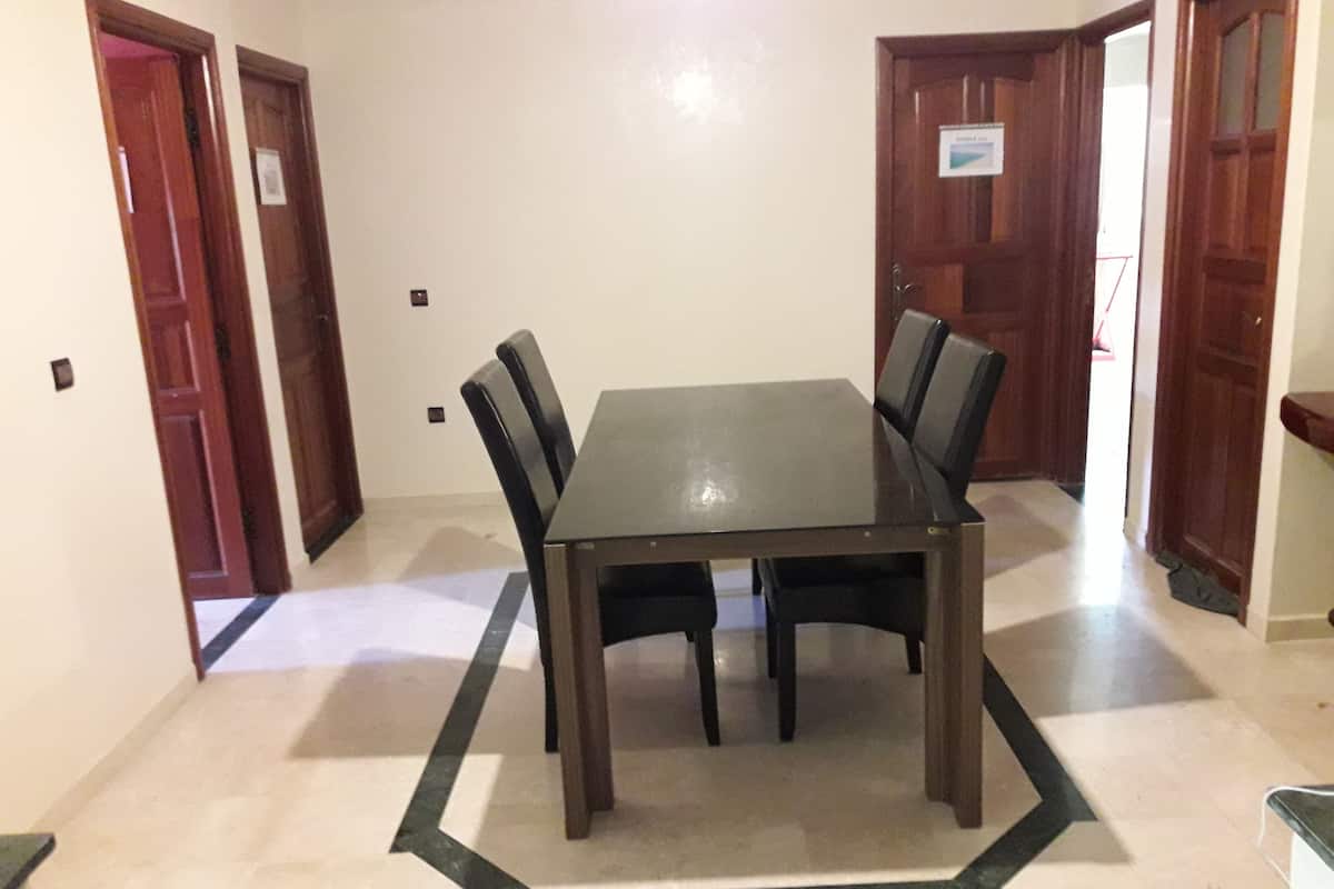 Ein Essbereich mit einem rechteckigen Tisch, umgeben von Stühlen, einem Fliesenboden und Holztüren.