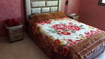 A bedroom with a floral bedspread, a headboard, a nightstand with a phone, and a red towel on the side table.