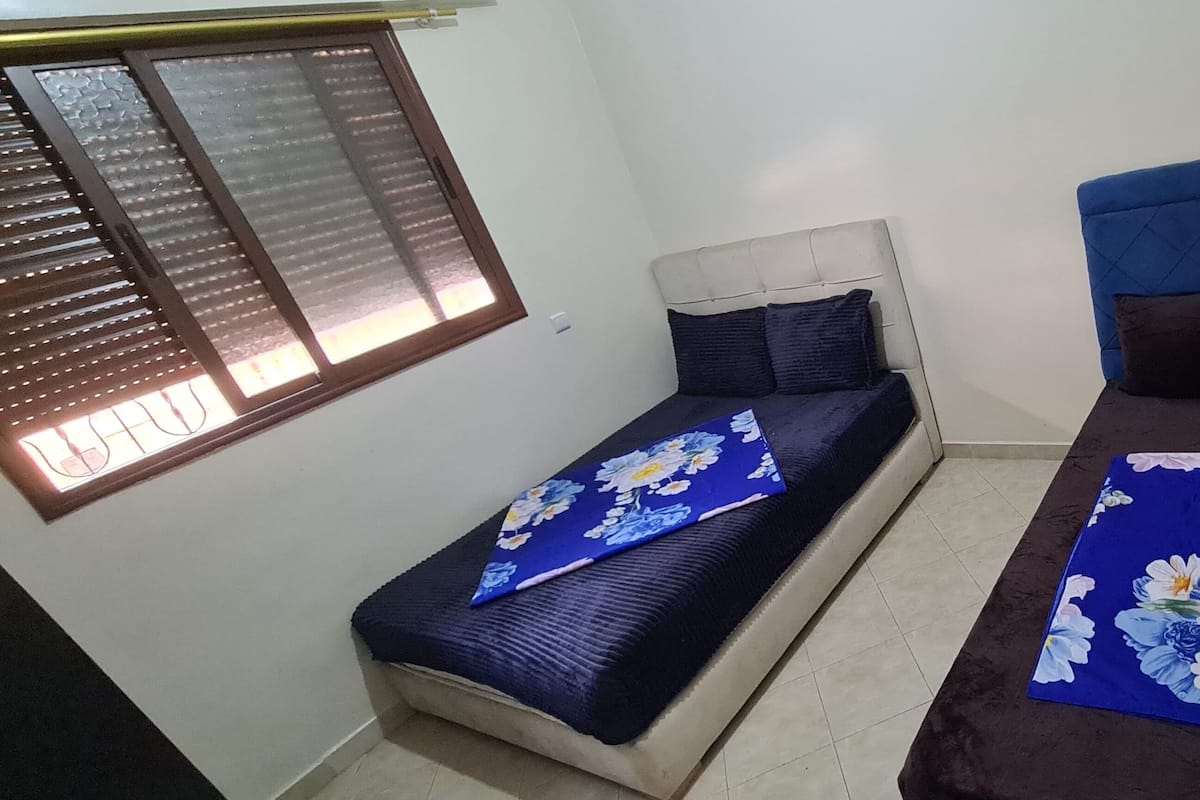 Ein kleines, gemütliches Zimmer mit zwei Einzelbetten, jeweils mit Kopfstütze und einer blumigen Tagesdecke.