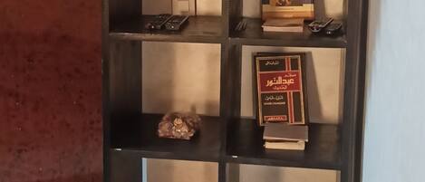 A black metal shelf with books, a remote control, and slippers.