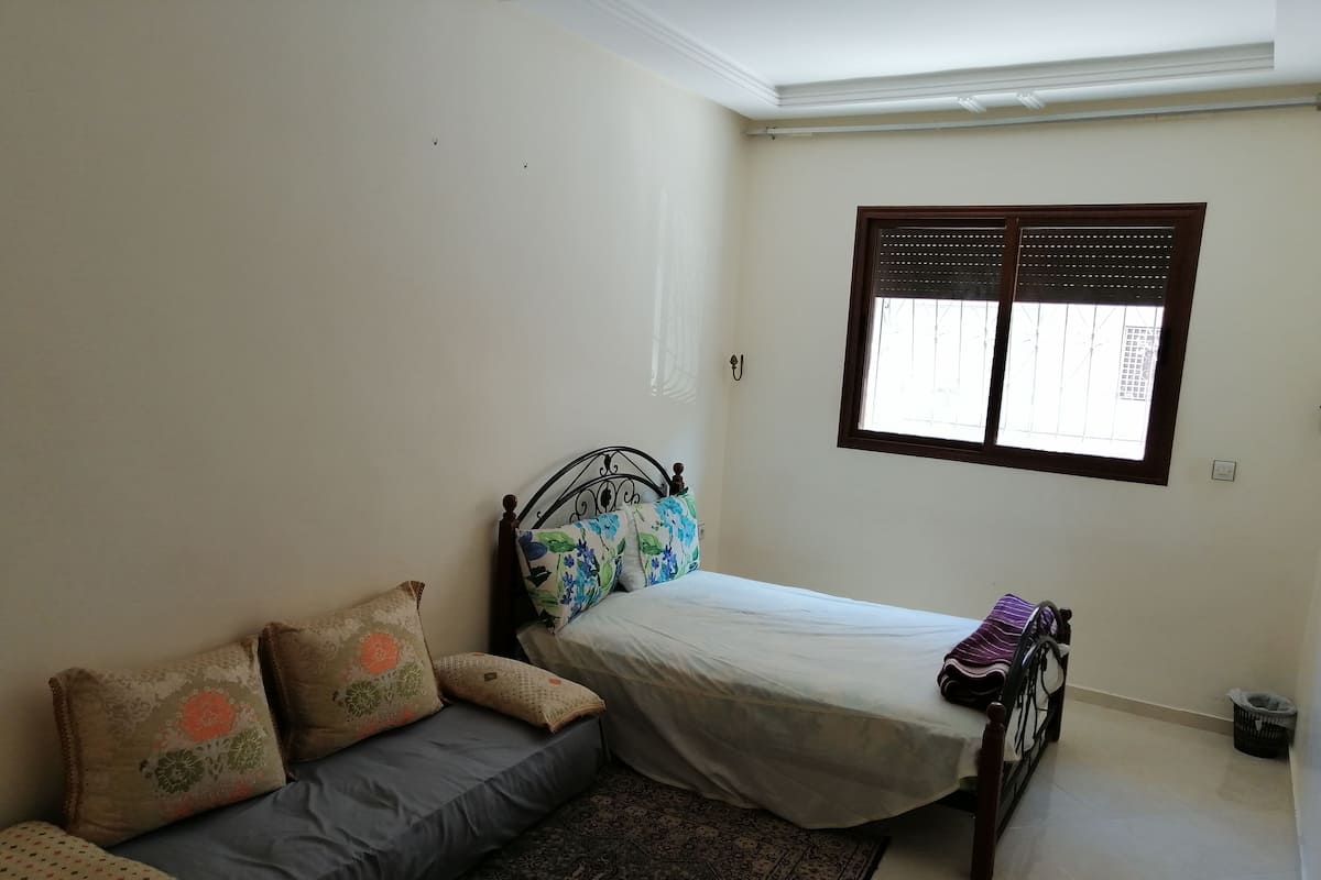 Ein Schlafzimmer mit Bett, Sofa, Fenster und einem gemusterten Teppich.