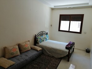 A bedroom with a bed, a sofa, a window, and a patterned rug.