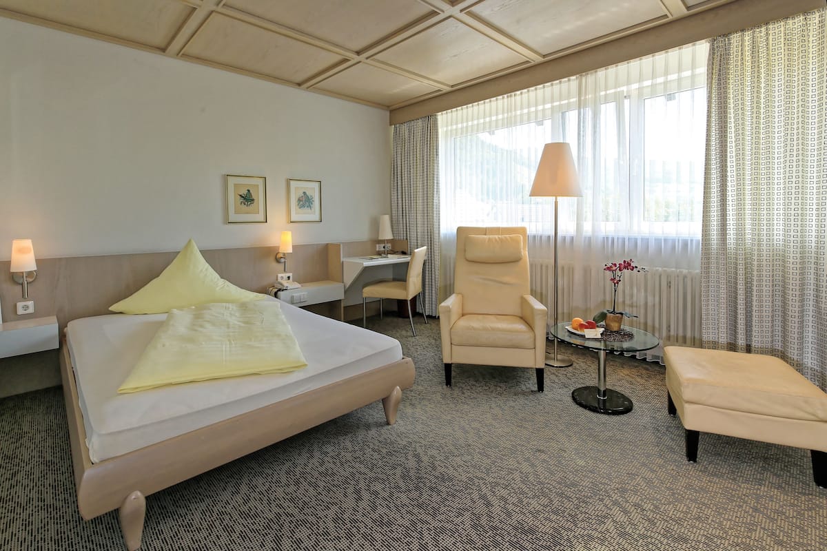 Een hotelkamer met een bed, een bureau, een stoel, een lamp en een klein tafeltje met bloemen.
