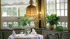A dining area with a table set for two, a chandelier, and potted plants. - Hotel Hirschen Glottertal (Glottertal)