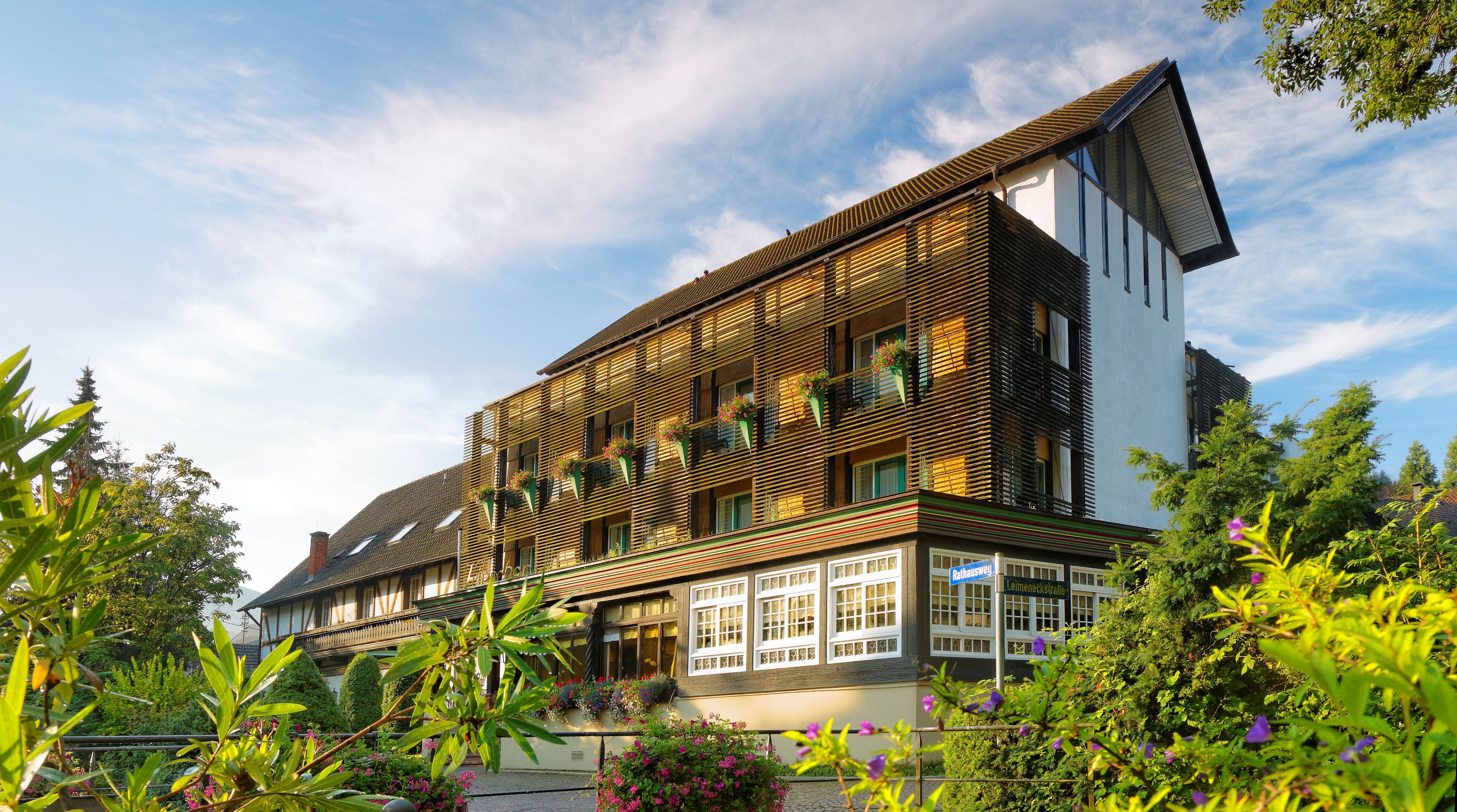 A multi-story hotel with a sloped roof, balconies with flower boxes, and a sign indicating the name and address.