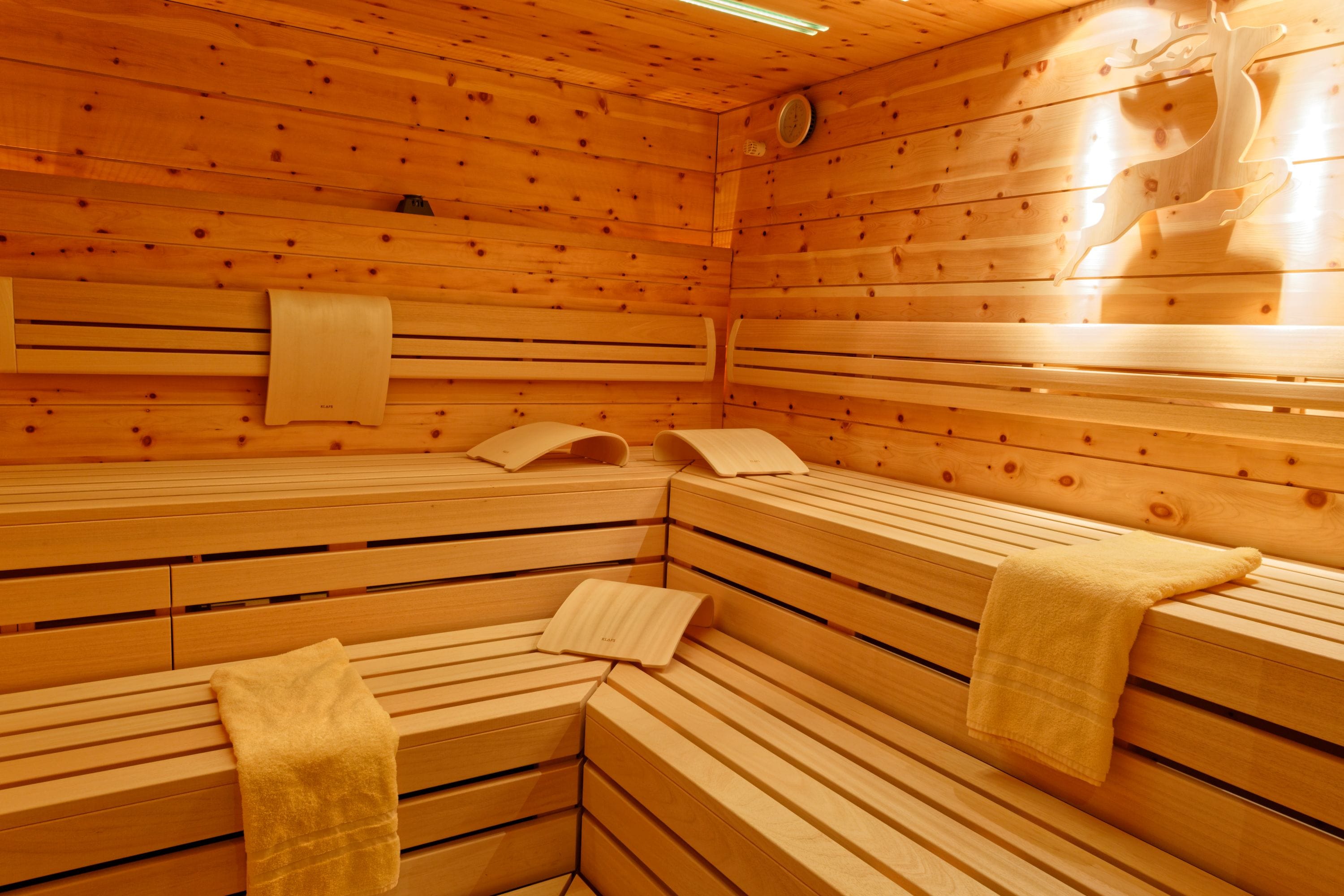 Sala de sauna con bancos de madera, toallas y un reloj en la pared.
