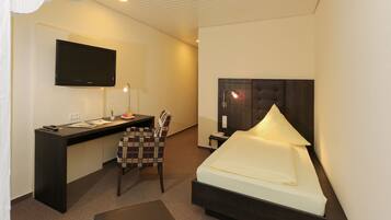 Una habitación de hotel con cama, escritorio, silla, televisión y mesita de noche.