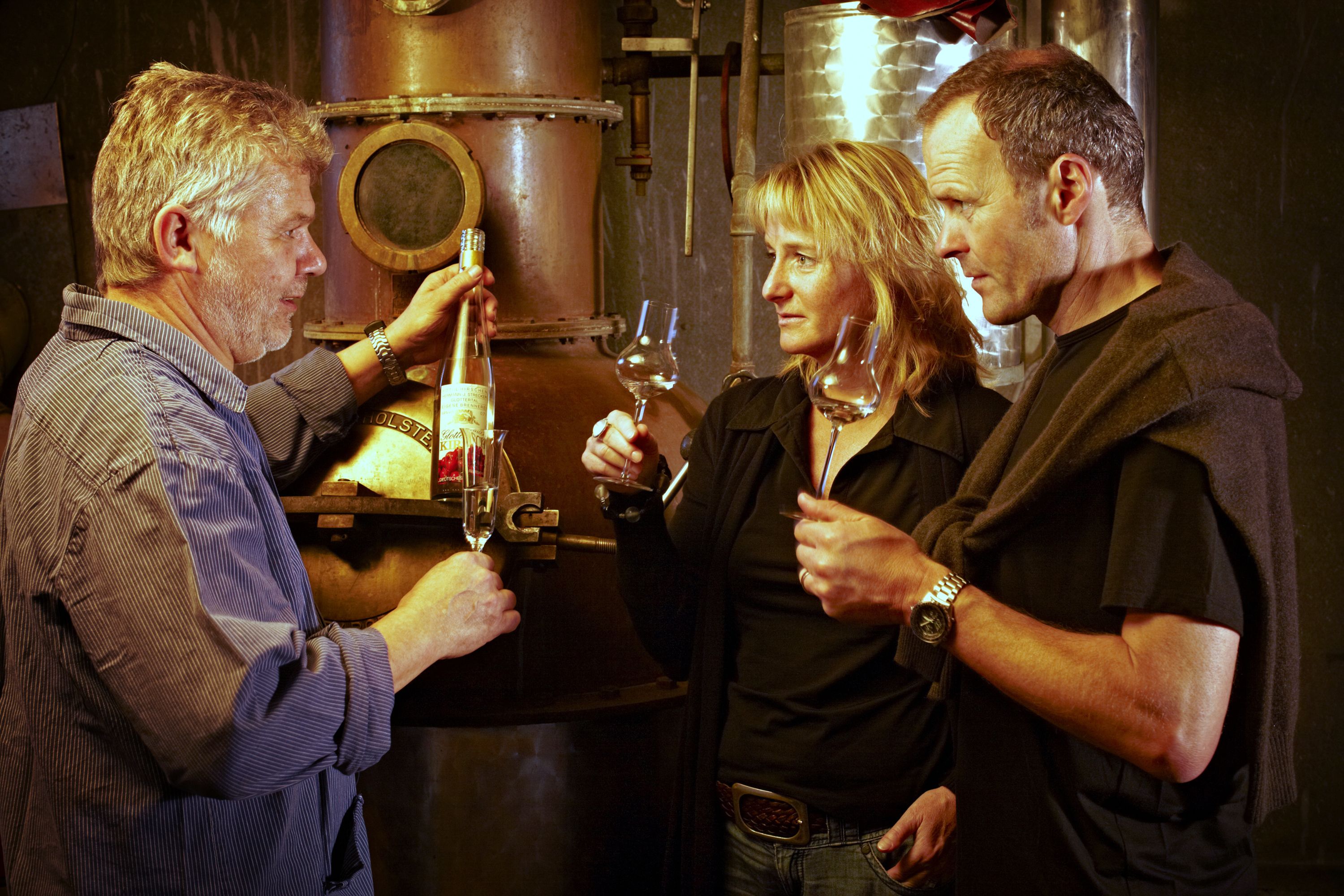 A group of people in a dimly lit room with industrial elements like metal tanks and pipes.