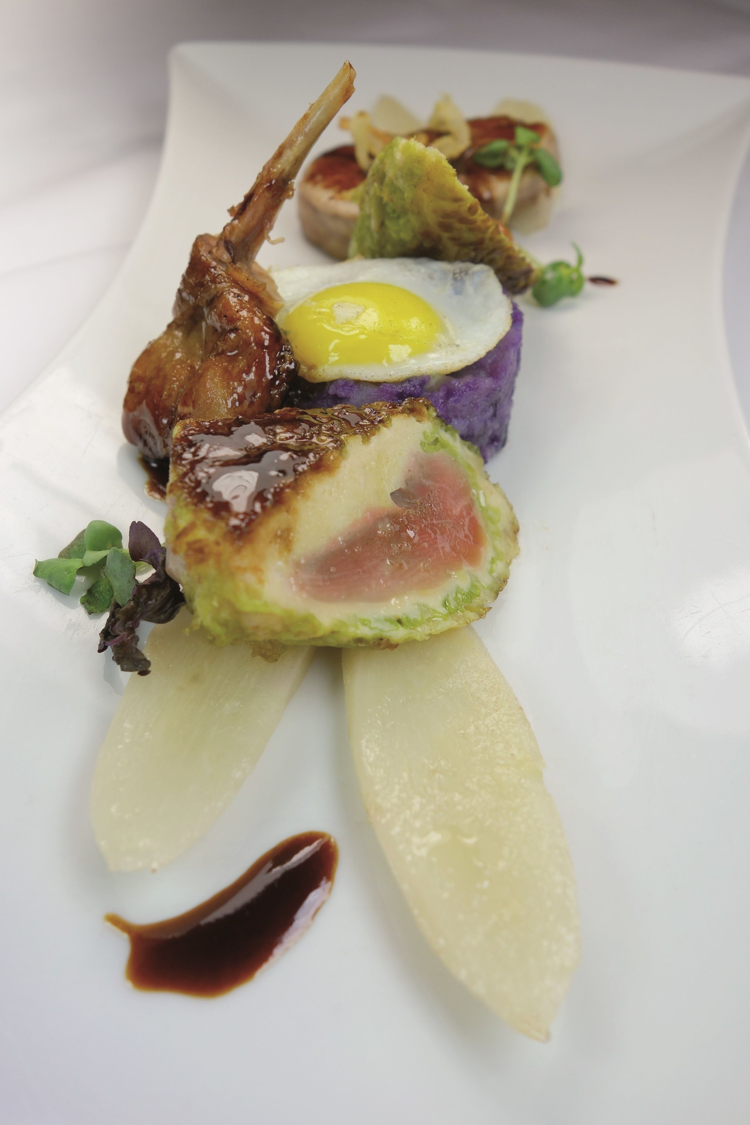 A white plate with a dish consisting of a grilled meat, a poached egg, and a purple vegetable.