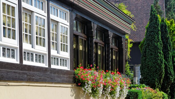 A building with large windows, a balcony with flowers, and a neatly trimmed hedge. - Hotel Hirschen Glottertal (Glottertal)