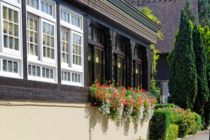 Un bâtiment doté de grandes fenêtres, d’un balcon orné de fleurs et d’un arbuste taillé avec soin.