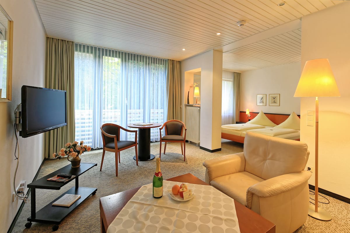 Een hotelkamer met een flatscreen televisie, een eettafel met een bloevas, een bank en een bed met nachtkastje.