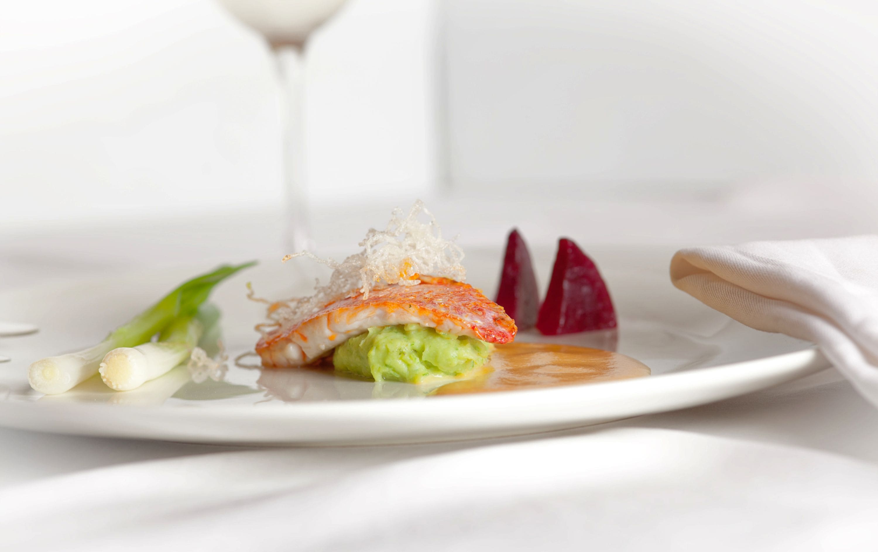A plate with a seafood dish, possibly sushi, garnished with green leaves and a clear liquid.