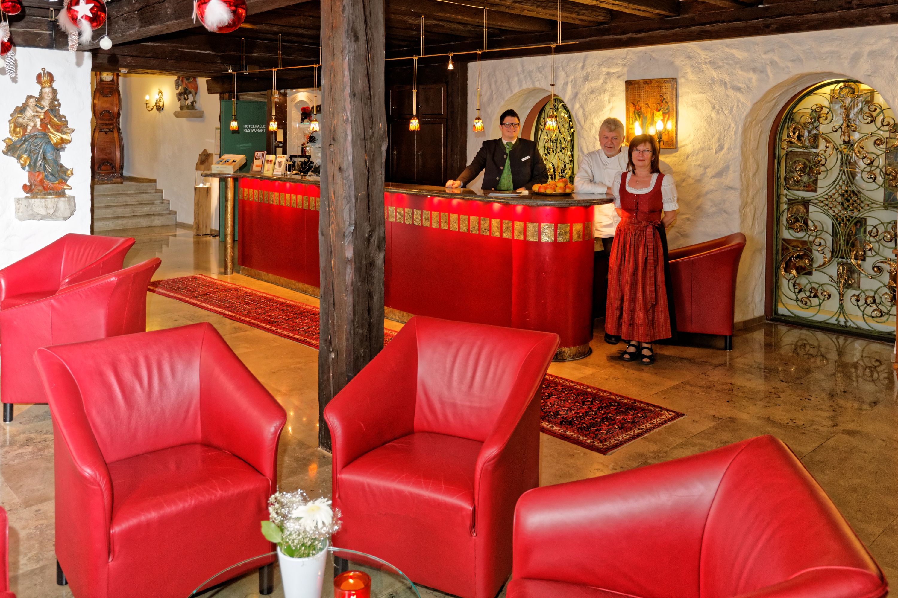 A hotel lobby with red leather chairs, a reception desk, and a decorative mirror.