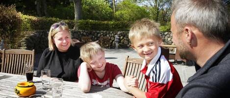 A family dining at an outdoor table with a stone wall and greenery in the background.