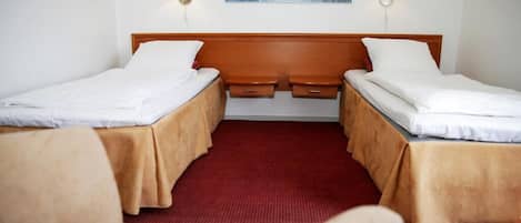 Een hotelkamer met twee enkele bedden, een houten hoofdbord, twee nachtkastjes en een rood tapijt.