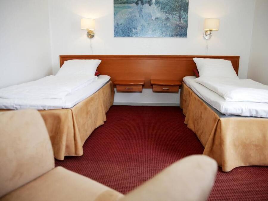 A hotel room with two single beds, a wooden headboard, two bedside tables, and a red carpet.