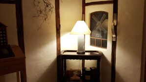 Una habitación con poca luz, una lámpara de mesa, un cuadro enmarcado y varios vasos de vino en el suelo.