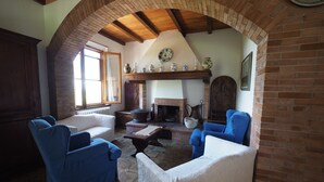 A cozy living room with a fireplace, blue armchairs, a white sofa, and a brick fireplace surround. - Fireplace, apartment with veranda and view of San Gimignano (San Gimignano)