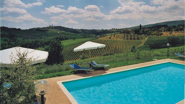 A swimming pool with lounge chairs and an umbrella, surrounded by lush green fields and a clear sky. - Fireplace, apartment with veranda and view of San Gimignano (San Gimignano)