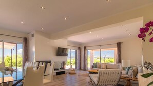 A spacious living area with a glass dining table, comfortable seating, a flat-screen TV, and large windows offering a view of the outdoors. - The Land, Villa-Finca 5StarsHome Mallorca (San Jordi)